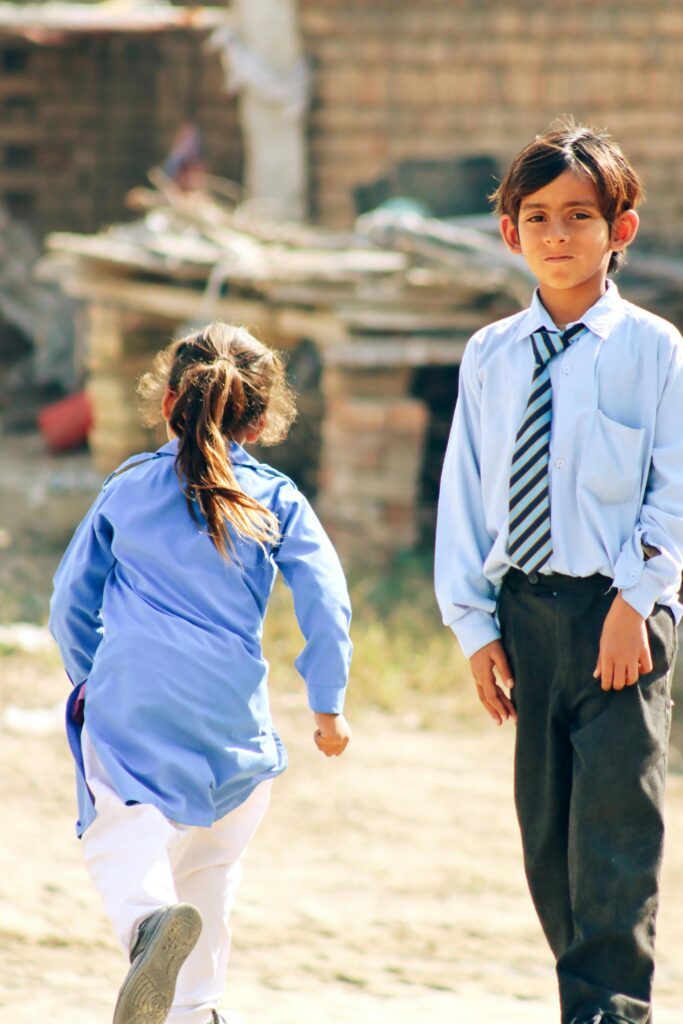 WE EDUCATE Children in school uniforms playing outdoors in a rural area of Pakistan.
